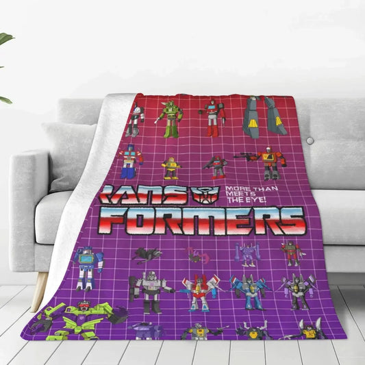 Couverture Transformers avec personnages robots colorés sur fond violet quadrillé, posée sur un canapé – Transformers.